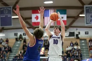 لاعب كرة سلة من فريق بورتلاند يسدد كرة نحو السلة، بينما يحاول لاعب غونزاغا الدفاع عنه. تظهر الأعلام في الخلفية.