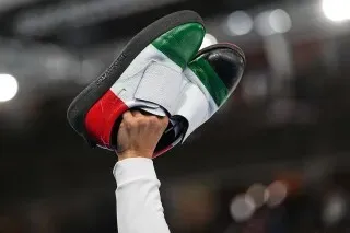 حذاء كيرلنج مرفوع بأيدٍ تحمل ألوان العلم الإيطالي، يعكس أهمية المعدات المتخصصة في رياضة الكيرلنج.