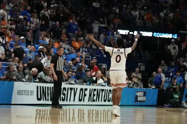 لاعب كرة سلة يحتفل بفوز فريقه في بطولة NCAA، بينما يشاهد الجمهور في الخلفية، مع لافتة تشير إلى استضافة البطولة في جامعة كنتاكي.