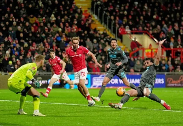 مباراة كرة قدم مثيرة بين ريكسهام وتشيلسي، حيث يتنافس اللاعبون على الكرة في ملعب مزدحم، مع حارس مرمى في وضعية التصدي.