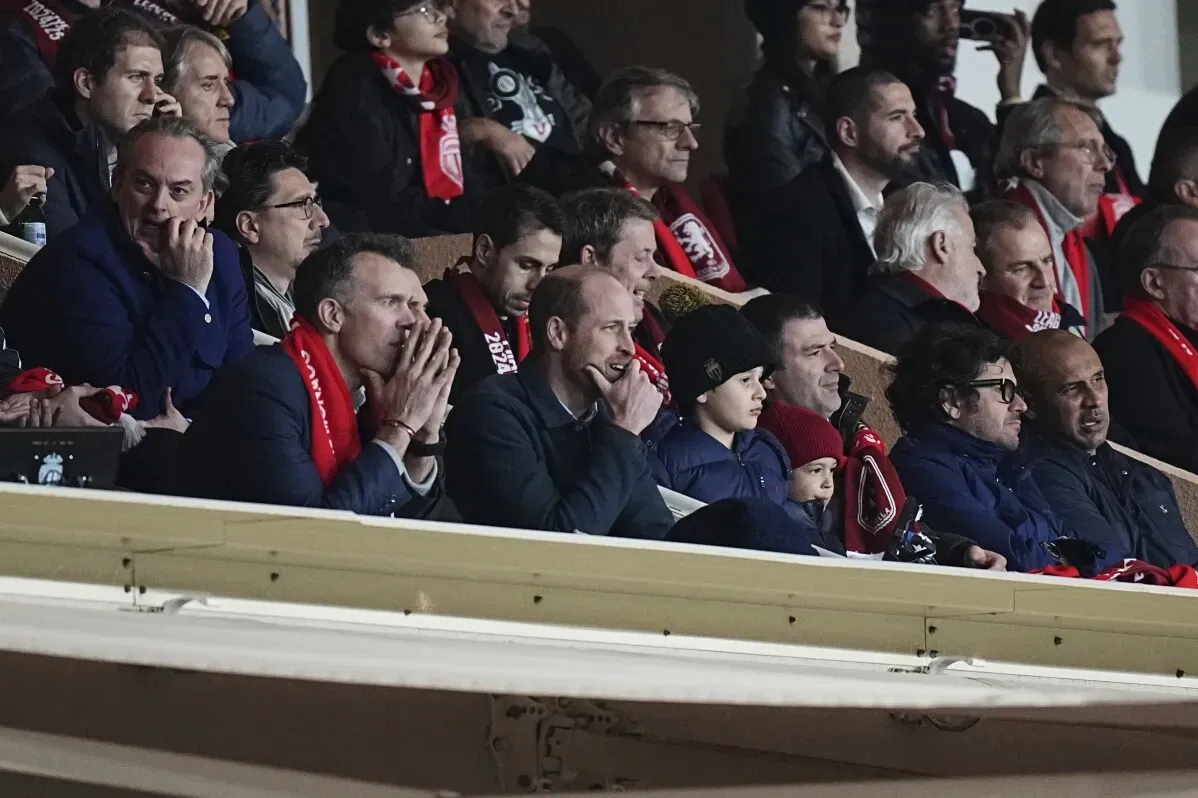 الأمير ويليام يشاهد مباراة أستون فيلا في دوري أبطال أوروبا بموناكو، محاطاً بالجماهير، يبدو جاداً ومهتماً بالمباراة.