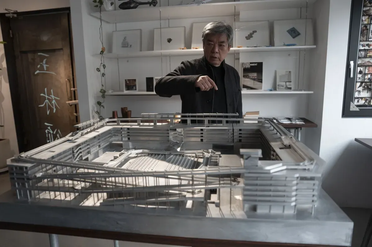 مهندس معماري صيني يُظهر نموذجًا لمشروعه في مكتبه، مع التركيز على تصميم مبتكر يوازن بين الاحتياجات التجارية والإنسانية.