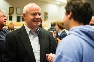 رجل يتحدث مع شخص آخر في تجمع اجتماعي، مع وجود أشخاص آخرين في الخلفية، يعكس تواصل المجتمع حول قضايا العدالة.