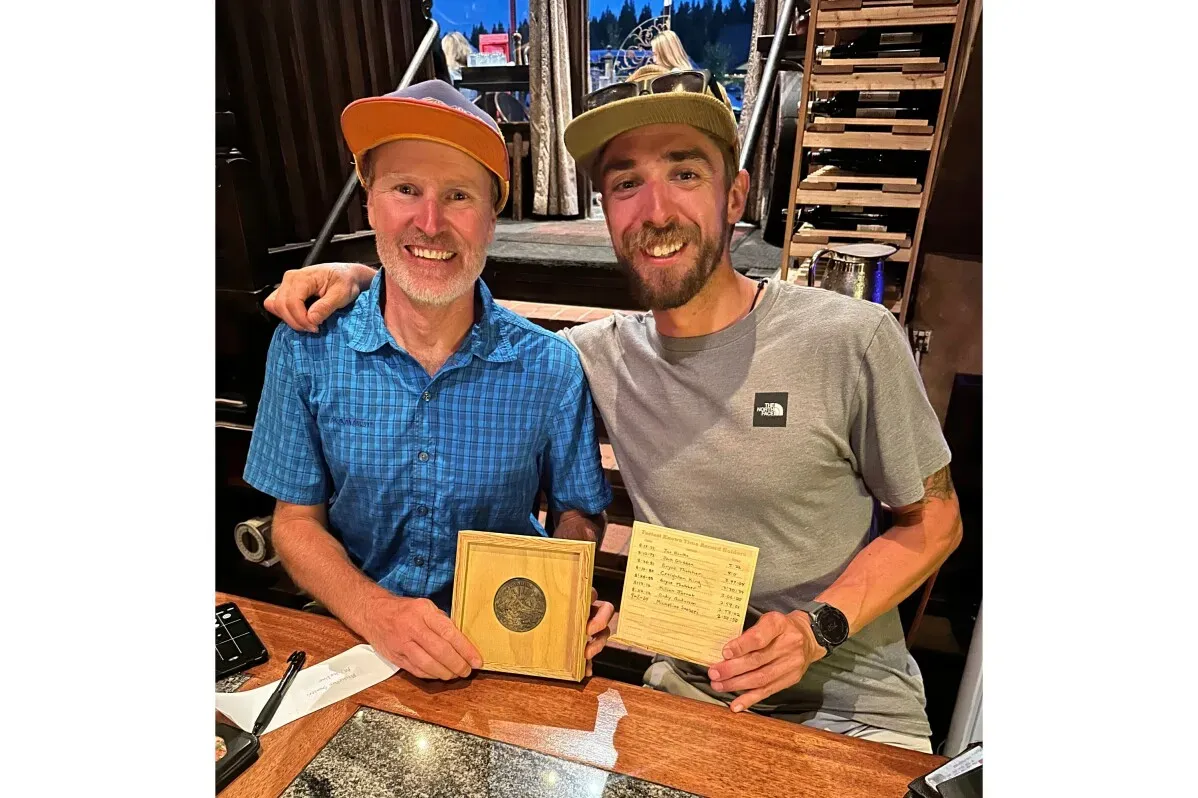 صورة لاثنين من المتسابقين يجلسان معًا في مطعم، يحمل أحدهما جائزة بينما يظهر الآخر مبتسمًا، مما يعكس احتفالًا بإنجاز رياضي.