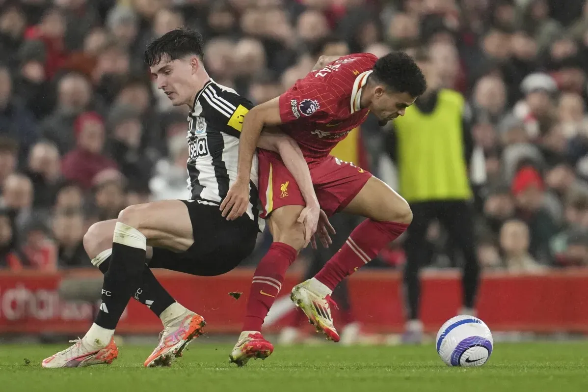 تدخل لاعب من ليفربول في التحام مع لاعب من نيوكاسل، مع وجود مشجعين في الخلفية، خلال مباراة في الدوري الإنجليزي الممتاز.
