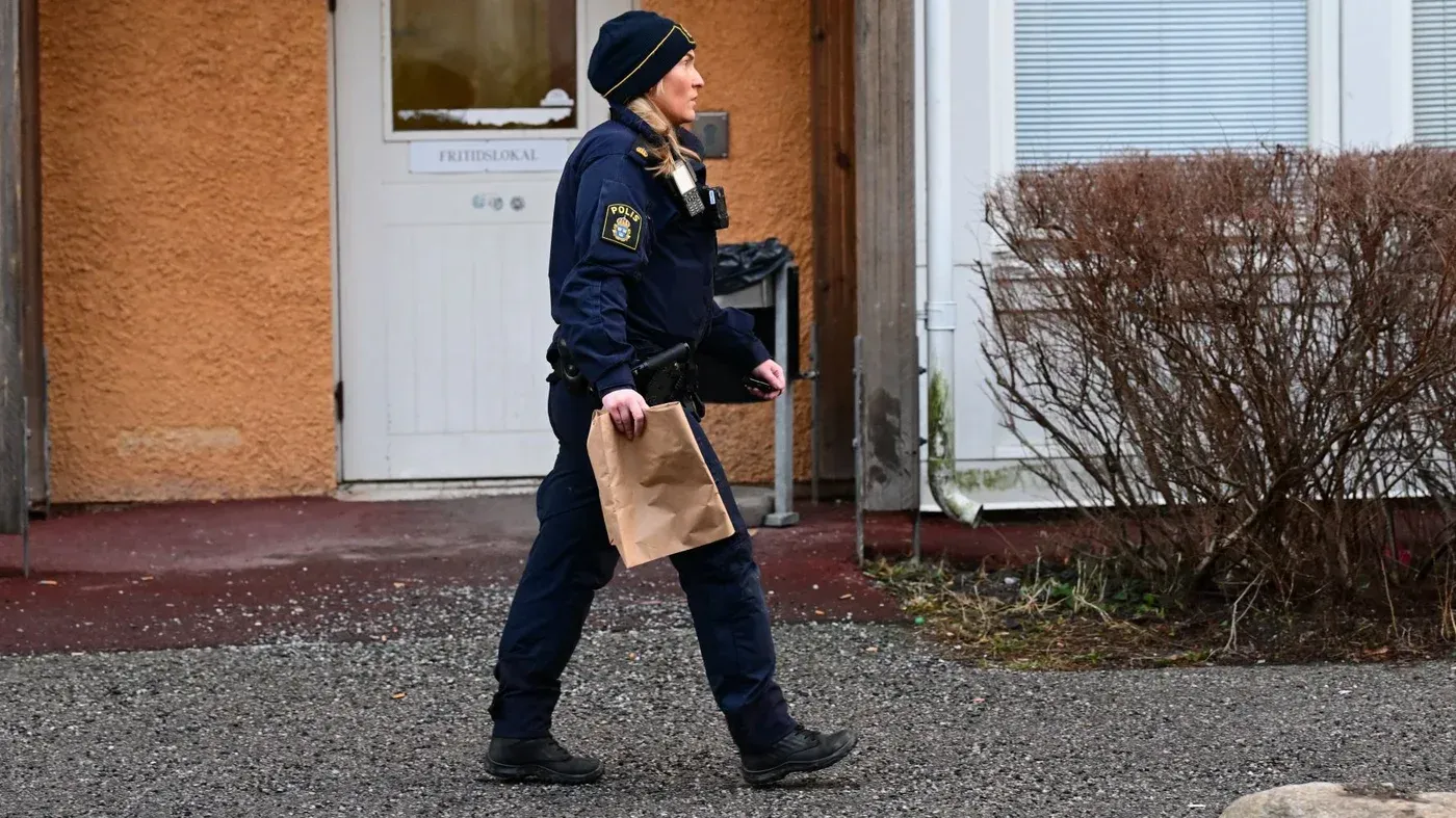 شرطية سويدية تحمل حقيبة ورقية أثناء وجودها في موقع حادثة مقتل الناشطة سلوان موميكا، وسط أجواء مشحونة بالتوتر.