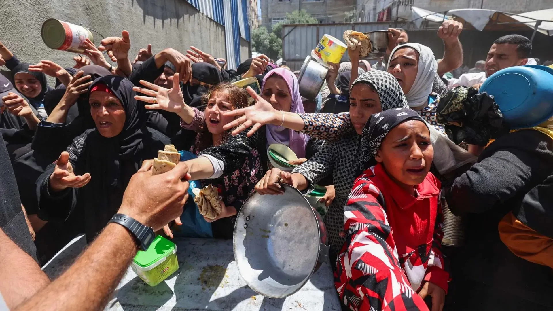 نساء وأطفال في غزة يتجمعون بقلق حول توزيع المساعدات الغذائية، مع تعبيرات يأس وأمل في الحصول على الطعام وسط أزمة إنسانية.