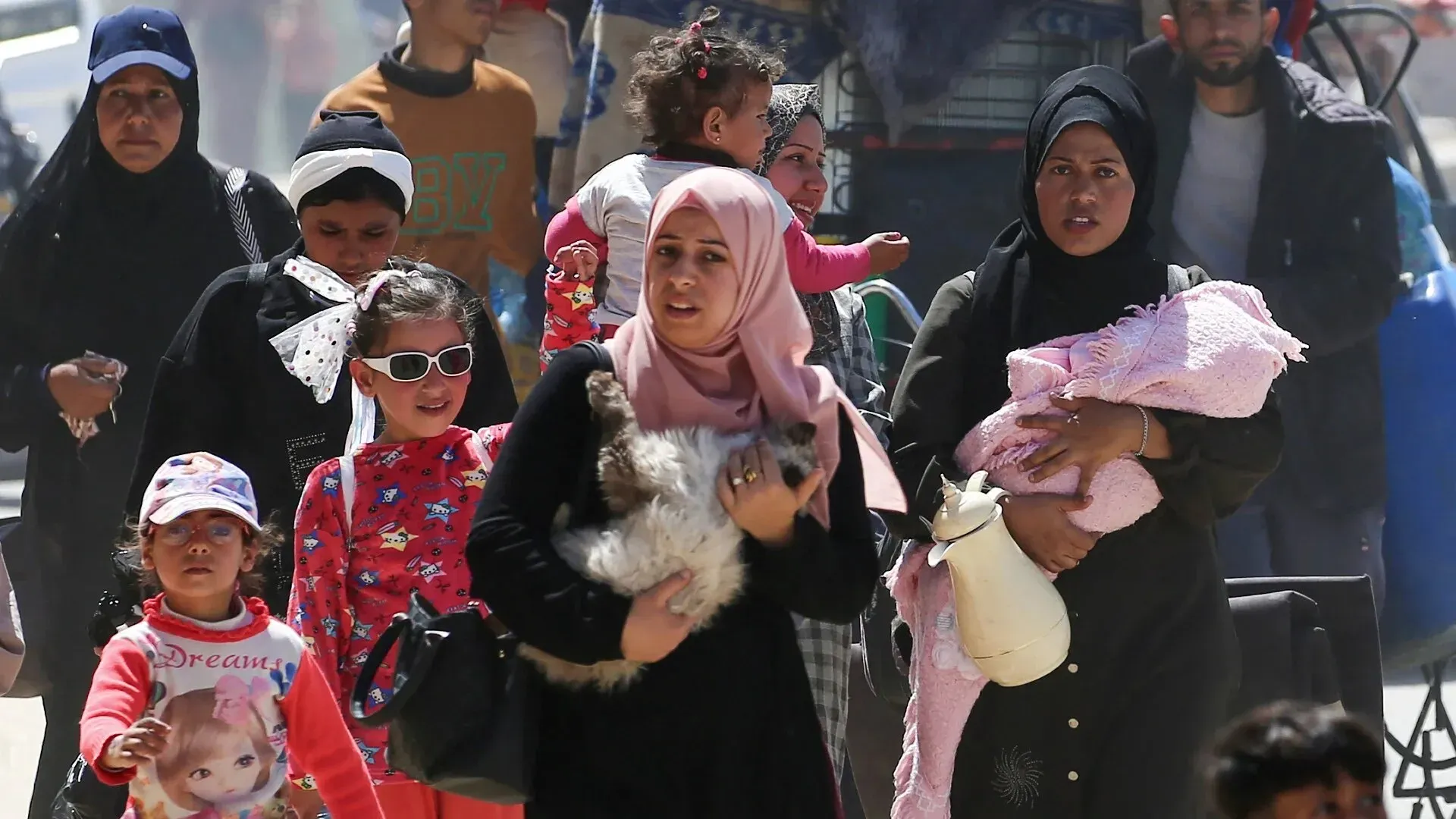نساء وأطفال فلسطينيون يتجمعون في منطقة مزدحمة، يعكسون معاناة النزوح والبحث عن ملاذ آمن في رفح بعد القصف.