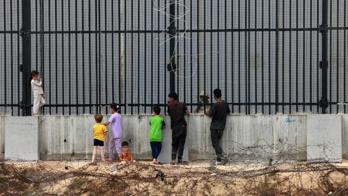 أطفال يقفون أمام سياج حديدي في رفح بغزة، يعبرون عن التحديات اليومية تحت الاحتلال، في سياق مقترح "مجتمع مخطط" جديد.
