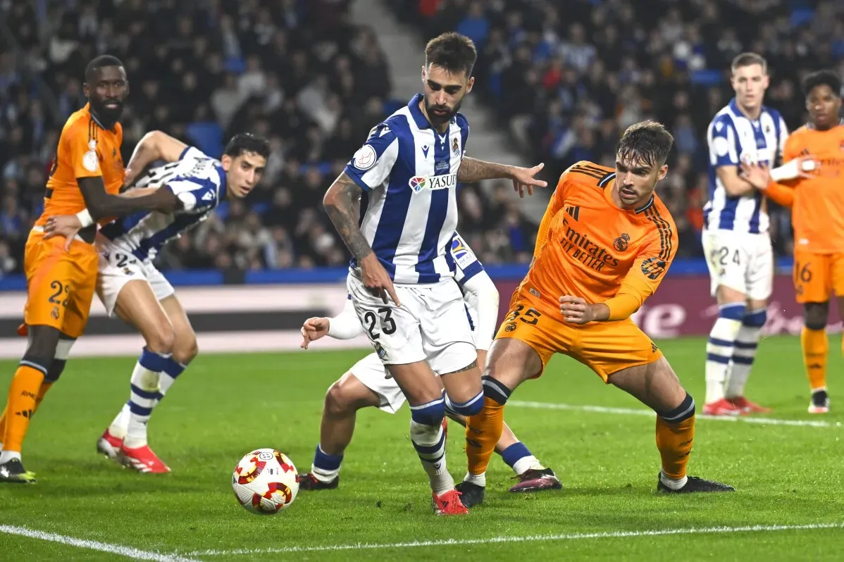 مباراة كرة قدم بين ريال سوسيداد وريال مدريد، حيث يتنافس اللاعبون على الكرة وسط أجواء مشحونة بهتافات جماهيرية.
