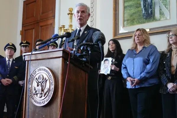 مشرع يتحدث أمام منصة في مجلس النواب، محاطاً بأفراد عائلات ضحايا حادث الطيران، مع صورة لأحد الضحايا في يده.