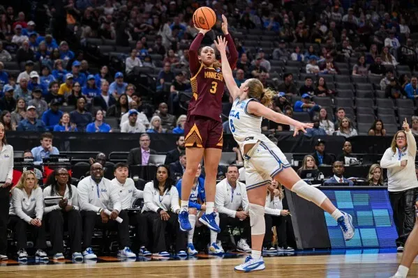 لاعبة كرة سلة من فريق مينيسوتا تسجل رمية ثلاثية بينما تحاول لاعبة من جامعة كاليفورنيا الدفاع عنها خلال مباراة في بطولة NCAA.