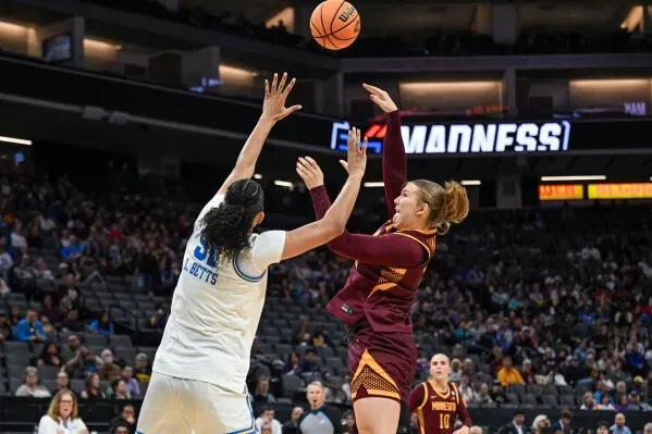 لاعبة كرة سلة من فريق مينيسوتا تسدد كرة بينما تحاول لاعبة فريق جامعة كاليفورنيا، لورين بيتس، الدفاع عنها في مباراة NCAA.