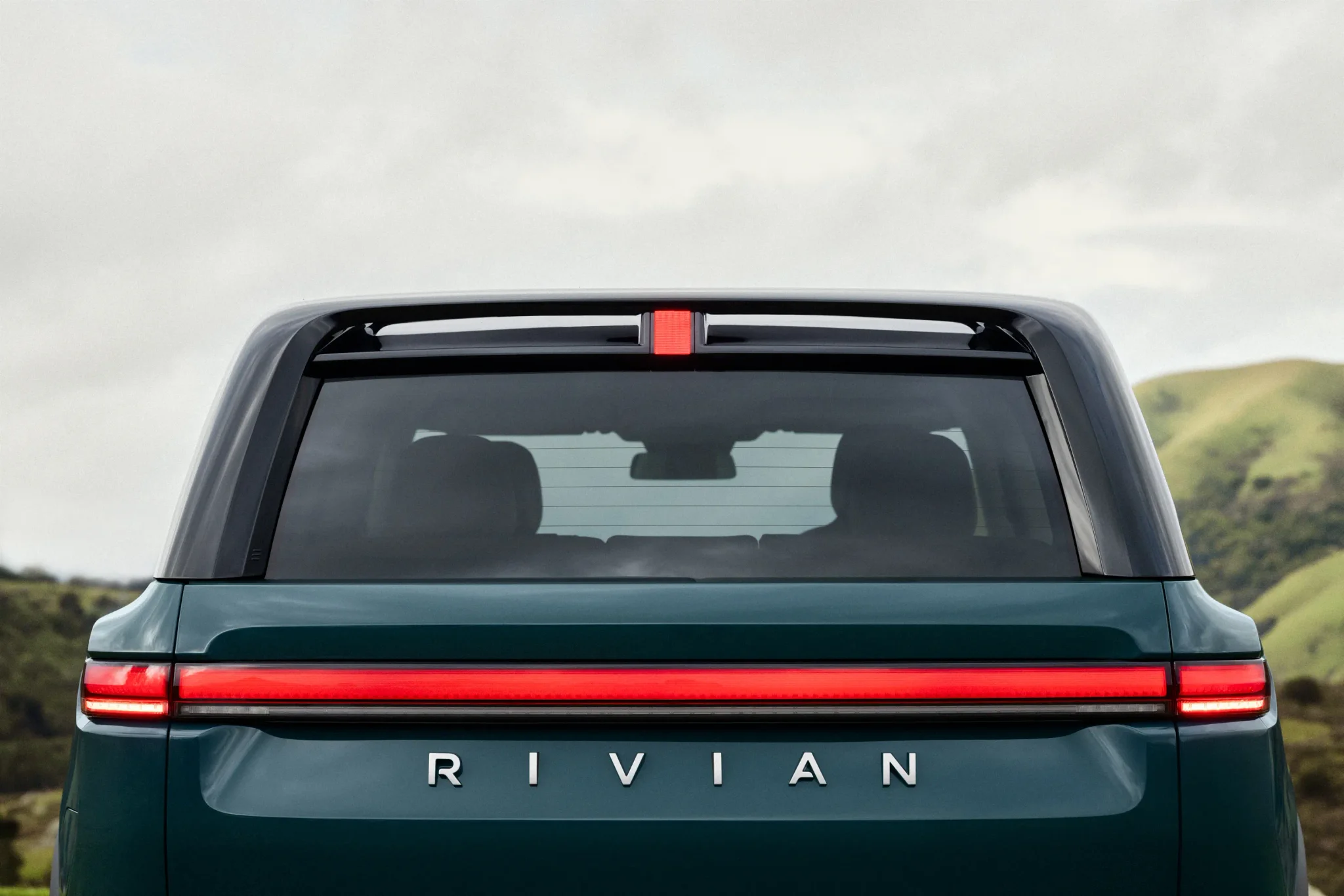 خلفية سيارة Rivian الكهربائية R2 باللون الأخضر مع شعار الشركة وإضاءة خلفية ممتدة، تعكس توسع الشركة في السوق الواسعة.