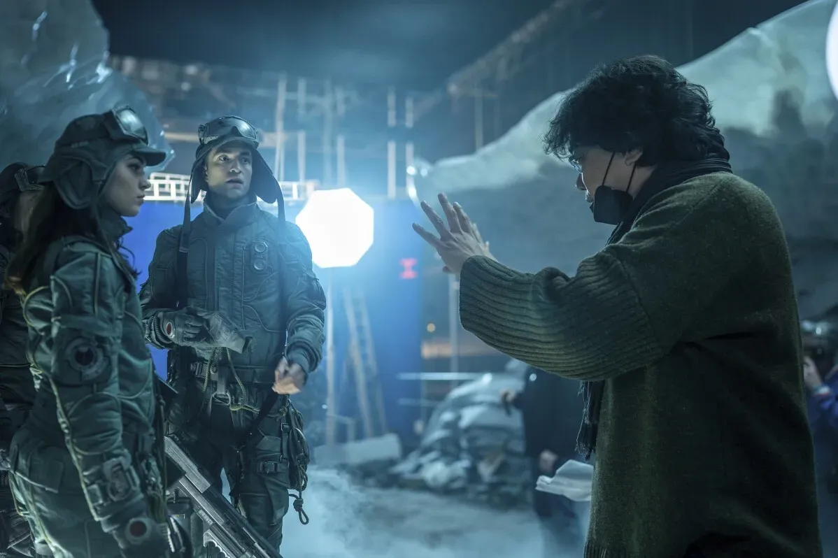 مشهد من فيلم "ميكي 17" يظهر المخرج بونغ جون هو مع طاقم العمل في موقع التصوير، وسط أجواء خيالية.