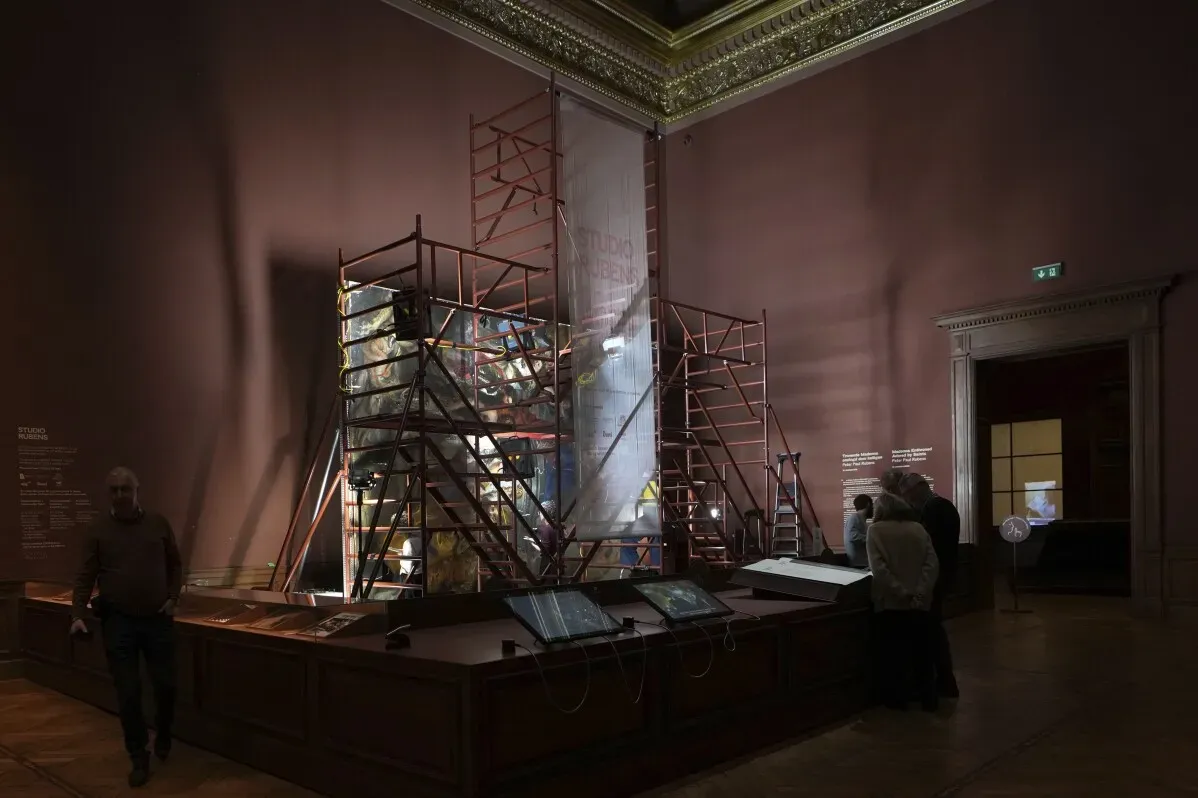 فريق من المرممين يعمل على ترميم لوحة "مادونا المتوجة المعشوقة من قبل القديسين" في متحف أنتويرب، محاطين بسقالات وأدوات الفنية.