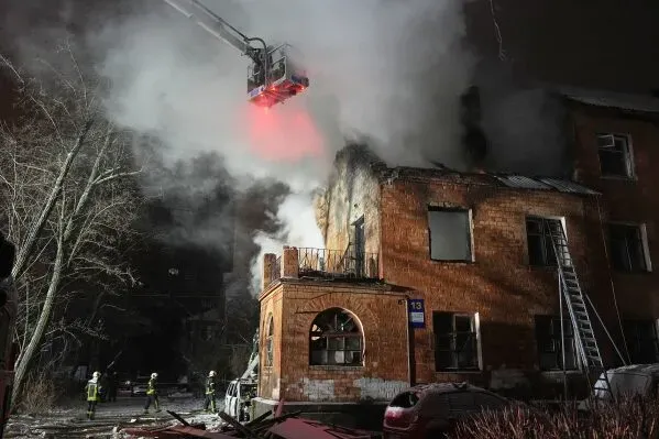 حريق ضخم في مبنى سكني في كييف، مع رجال الإطفاء يستخدمون السلم لإخماد النيران والدخان يتصاعد من السقف.