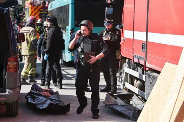 رجال إنقاذ وأفراد من الشرطة يعملون في موقع غارة روسية على دنيبرو، مع وجود جثث مغطاة في الخلفية وأجواء توتر بعد الهجوم.