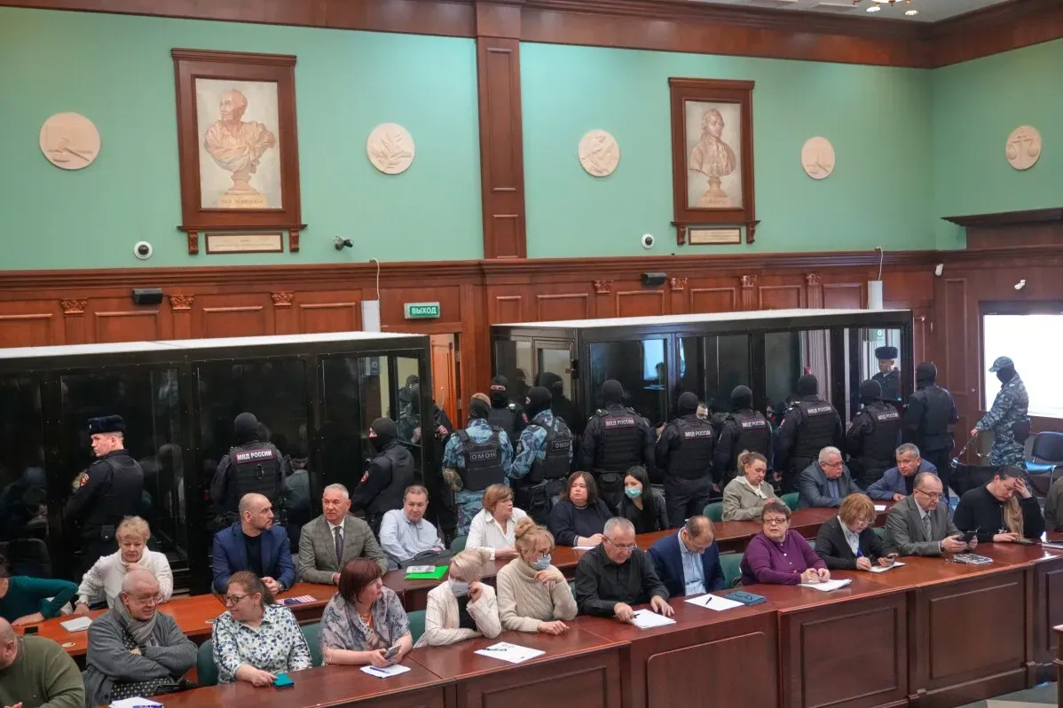 محكمة في موسكو تشهد محاكمة 19 شخصًا متورطين في هجوم مسلح أسفر عن مقتل 149 شخصًا، مع وجود قوات الأمن في الخلفية.