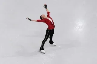 أديليا بيتروسيان، المتزلجة الروسية، تؤدي حركة راقصة على الجليد أثناء المنافسة في أولمبياد ميلانو، مرتدية زيًا أحمر.