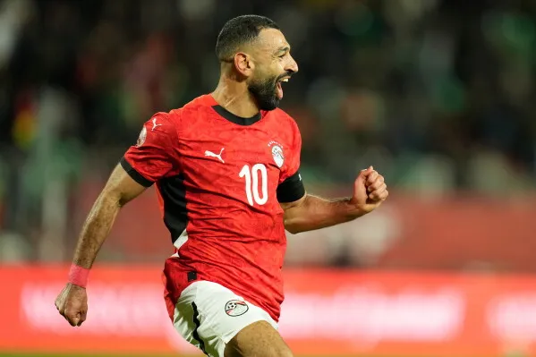 محمد صلاح يحتفل بفوز فريقه مصر، مرتديًا القميص رقم 10، مع تعبير عن الفرح بعد تسجيل هدف مهم في مباراة حاسمة.