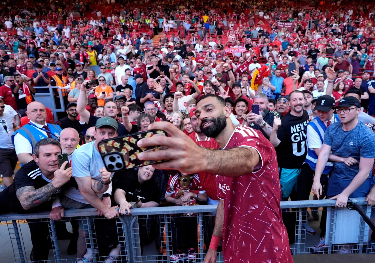 محمد صلاح يلتقط سيلفي مع جماهير ليفربول في ملعب أنفيلد، حيث يحتفلون بإنجازاته بعد تسع سنوات من التألق في النادي.