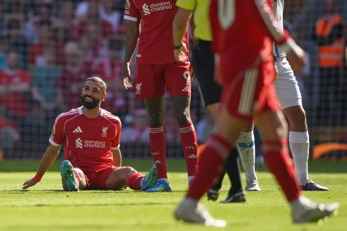محمد صلاح جالس على أرض الملعب بعد إصابته في مباراة ليفربول، مع زملائه في الفريق خلفه، مما يعكس تحديات الموسم الحالي.