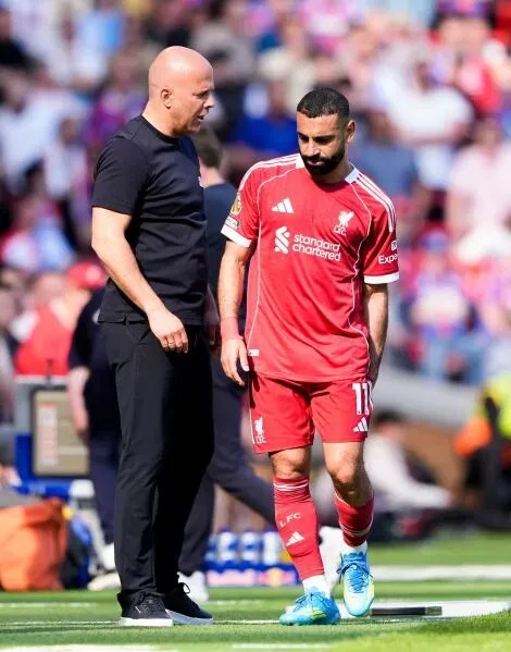 محمد صلاح، لاعب ليفربول، يتحدث مع مدربه بعد إصابته في مباراة سابقة، حيث يستعد للوداع في أنفيلد قبل مغادرته النادي.