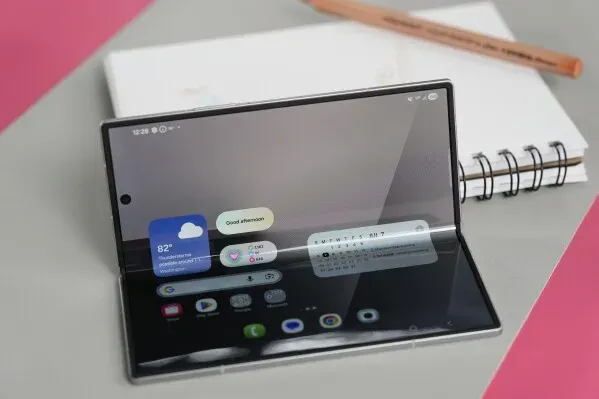 هاتف Galaxy Z Fold 7 القابل للطي مفتوح، يظهر شاشته الكبيرة مع واجهة مستخدم، بجانب دفتر ملاحظات وقلم.