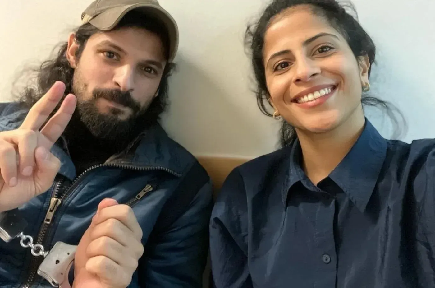 عبد الرحمن الخالدي، مدافع سعودي عن حقوق الإنسان، يظهر مبتسمًا مع شخص آخر، بينما يُظهر يده المربوطة بالأصفاد، مما يعكس وضعه الصعب في بلغاريا.