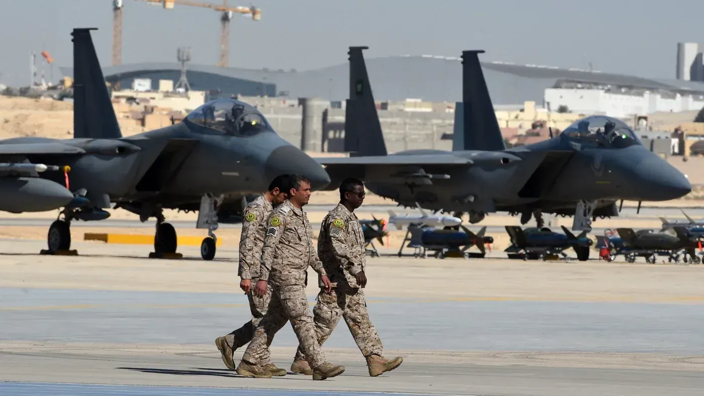 جنود سعوديون يسيرون بجوار طائرات مقاتلة من طراز F-15 في قاعدة عسكرية، مما يعكس تحديث القدرات الدفاعية للمملكة.