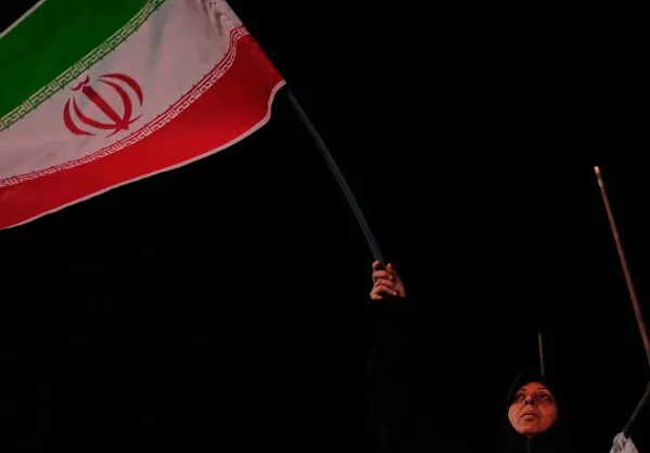 امرأة ترفع علم إيران في مظاهرة ليلية تعكس التوترات السياسية والعمليات العسكرية في المنطقة الخليجية.