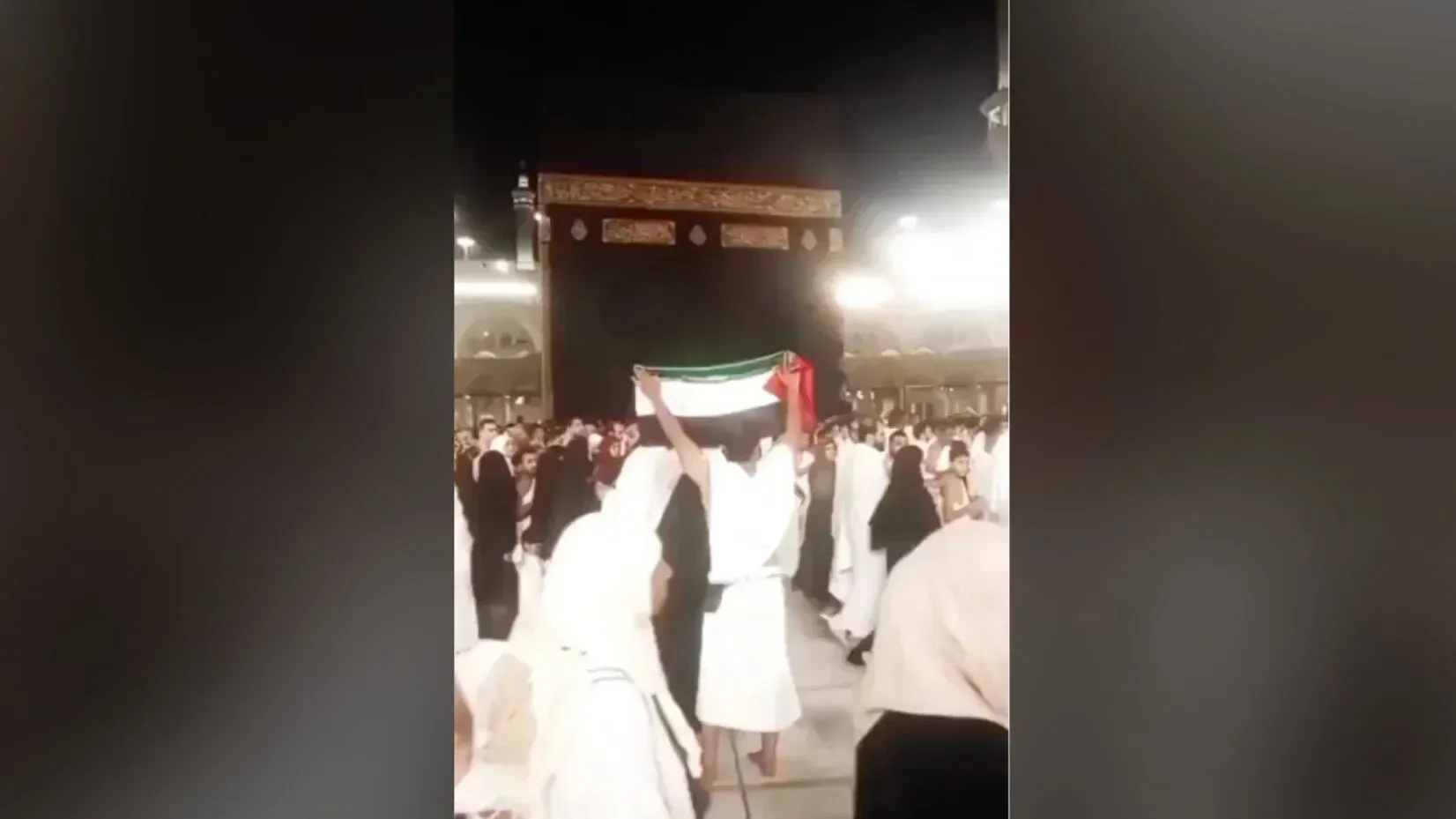 رجل يحمل علم فلسطين في المسجد الحرام بمكة المكرمة، وسط حشود من الحجاج، أثناء مناشدته لإنهاء حصار غزة.
