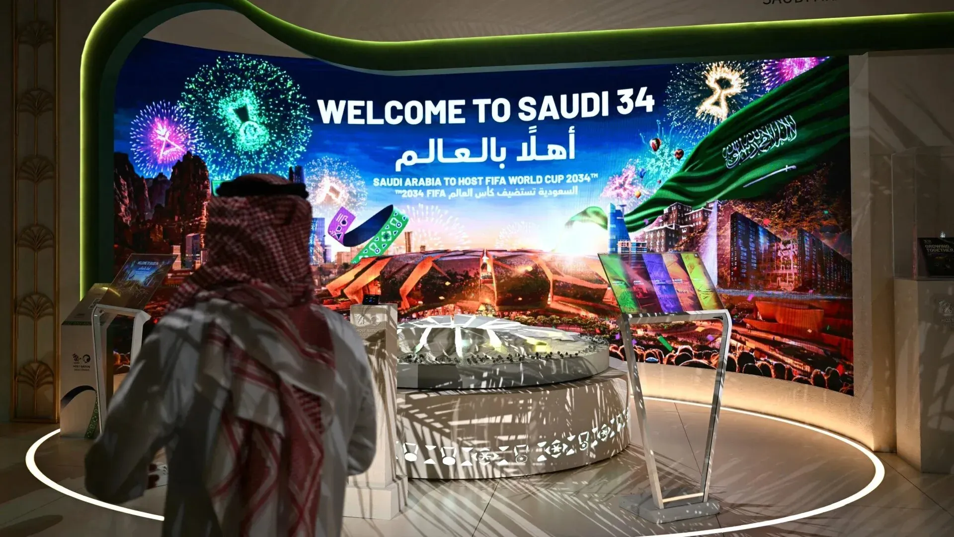 واجهة ترحيبية لكأس العالم 2034 في السعودية، مع عرض للألعاب النارية وعلم المملكة، تعكس الاستعدادات لاستضافة البطولة.