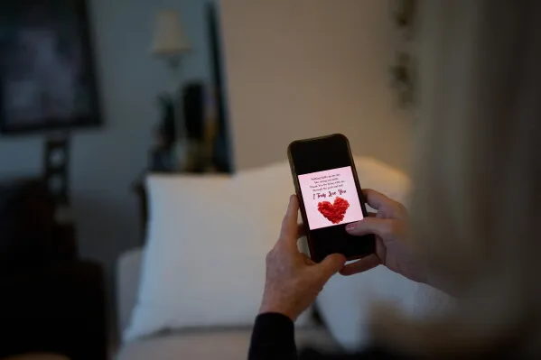 شخص يحمل هاتفًا يعرض رسالة حب مزيفة تعكس عمليات الاحتيال الرومانسية عبر الإنترنت وخسائر الضحايا المالية.