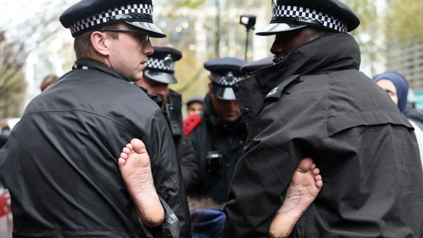 شرطيان يحملان لافتة تُظهر أقدامًا مكشوفة، أثناء احتجاج دعمًا لسجين فلسطيني مضرب عن الطعام خارج سجن وورموود سكربس في لندن.