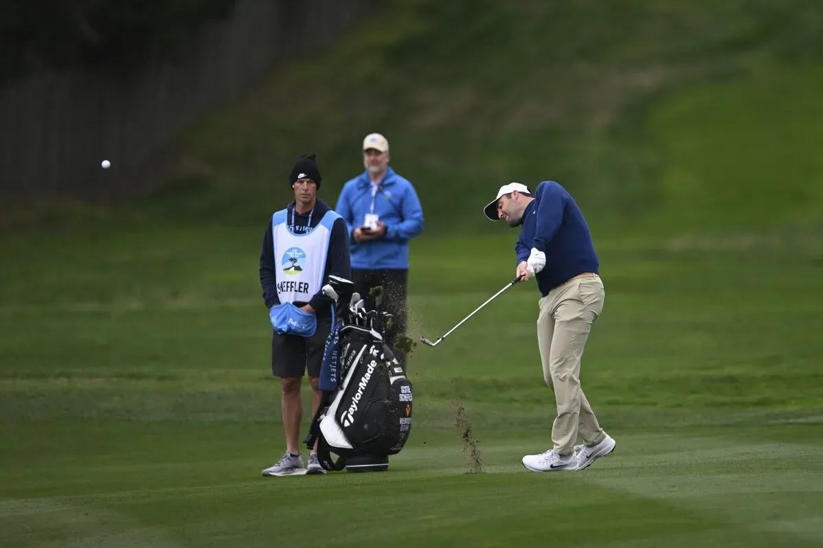 سكوتي شيفلر أثناء تسديد الكرة في بطولة AT&T Pebble Beach Pro-Am، مع وجود موظف يحمل حقيبة الجولف بملبسه الشتوي خلفه.