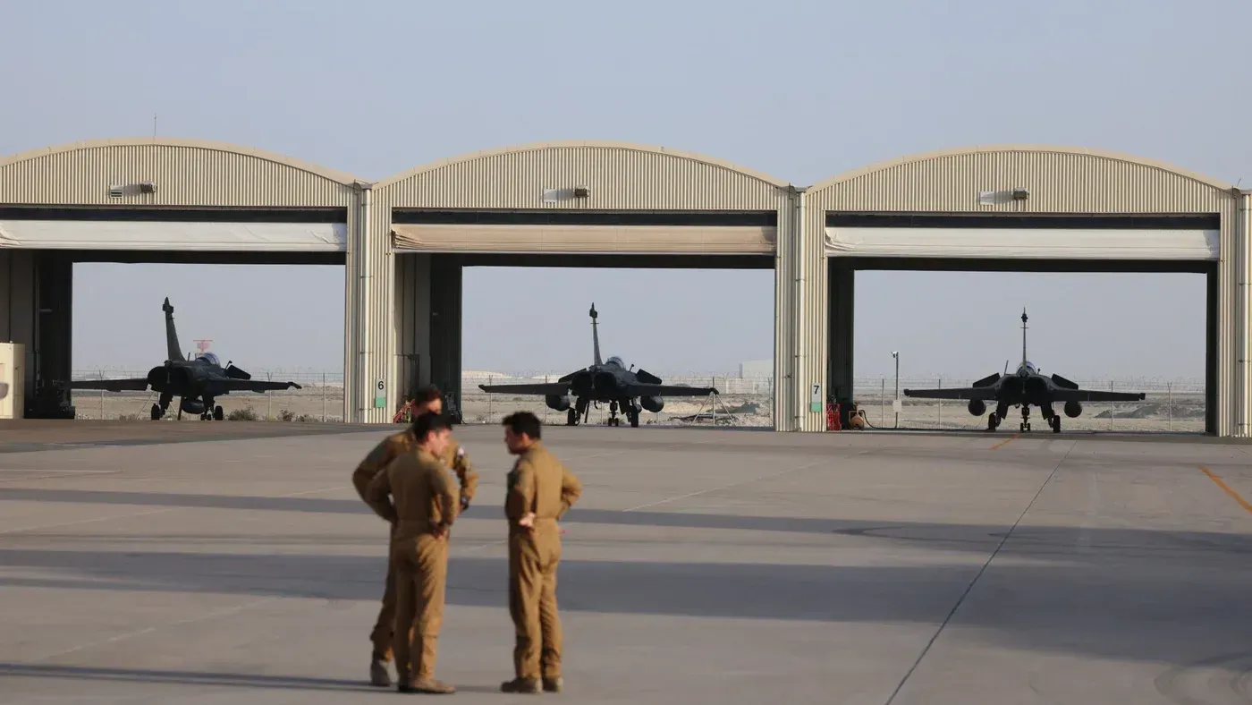تظهر الصورة طائرات حربية في قاعدة جوية بالإمارات، مع وجود جنود يتحدثون في المقدمة، مما يعكس التوترات العسكرية الحالية في المنطقة.