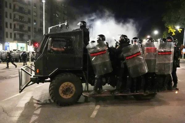 عربة شرطة محملة بعناصر مكافحة الشغب في بلغراد، وسط أجواء متوترة خلال الاحتجاجات ضد الحكومة، مع دخان يتصاعد في الخلفية.