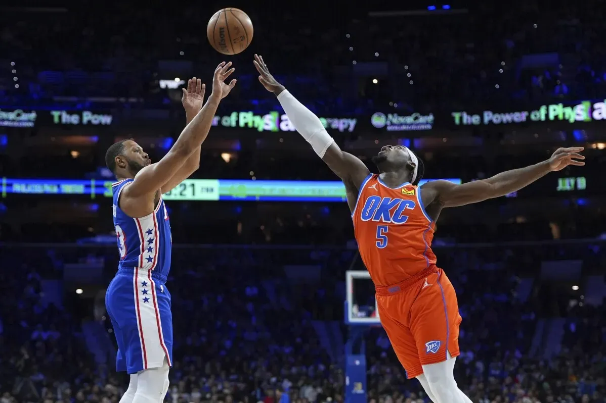 لاعب من فريق فيلادلفيا 76ers يسجل رمية ثلاثية بينما يحاول لاعب من أوكلاهوما سيتي ثاندر الدفاع عنه، في مباراة مثيرة.