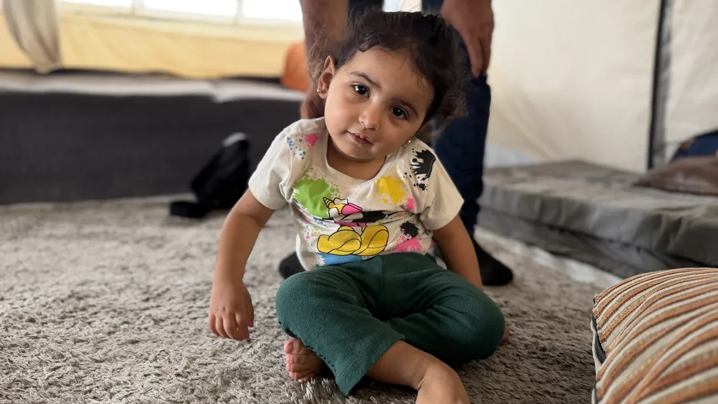 نور أبو سمعان، طفلة فلسطينية، تجلس على الأرض في خيمة، تعكس آثار الحرب والمعاناة، بعد نجاتها من قصف مستشفى في غزة.
