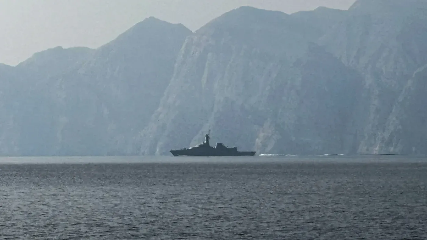 سفينة حربية تبحر في مياه مضيق هرمز، محاطة بالجبال، في ظل تصاعد التوترات بين إيران والولايات المتحدة.