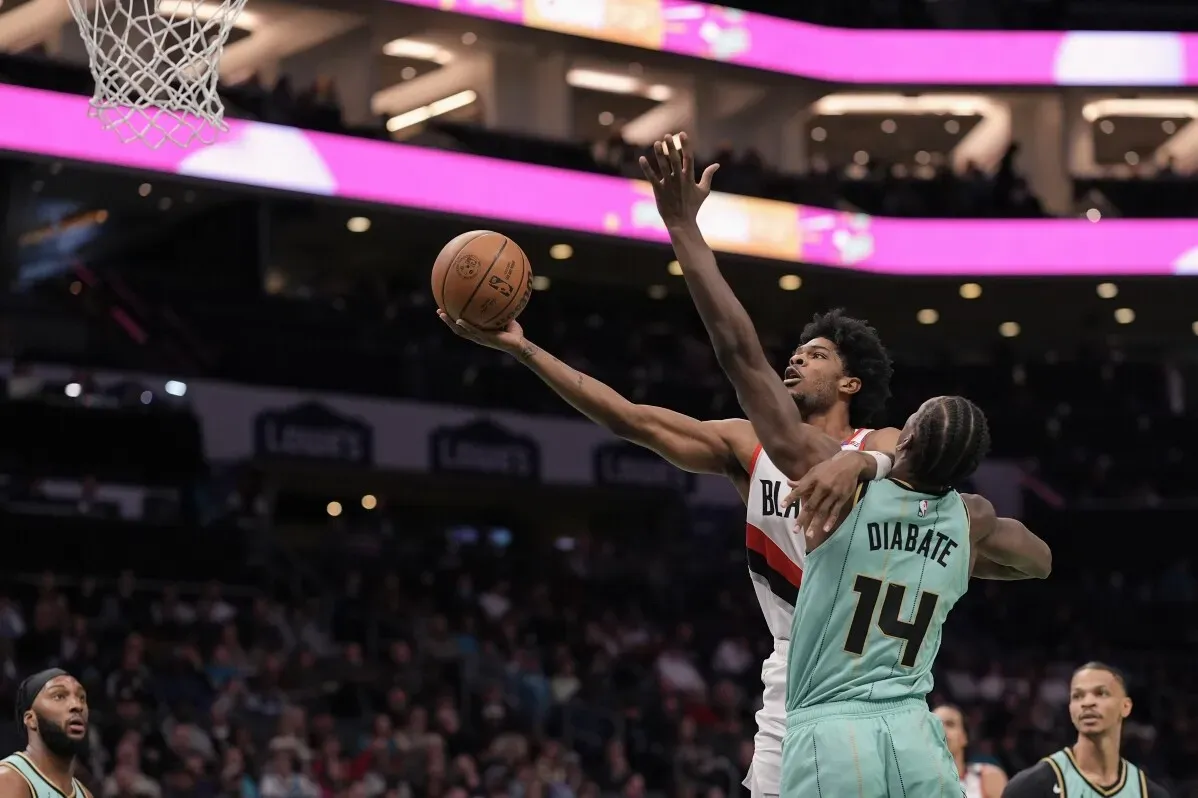تسديدة قوية من لاعب بورتلاند تريل بليزرز بينما يواجه دفاع لاعب تشارلوت هورنتس، مع أجواء ملعب حماسية في الخلفية.