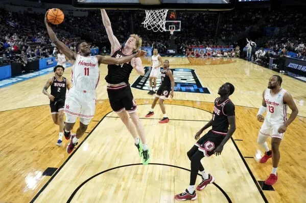لاعب كرة سلة من فريق هيوستن يسجل نقطة خلال مباراة NCAA ضد فريق SIU Edwardsville، مع تفاعل اللاعبين في الخلفية.