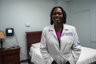 طبيبة أعصاب مبتسمة ترتدي معطفًا أبيض في غرفة نوم مخصصة للدراسات، تشير إلى أهمية فهم بيانات تتبع النوم.