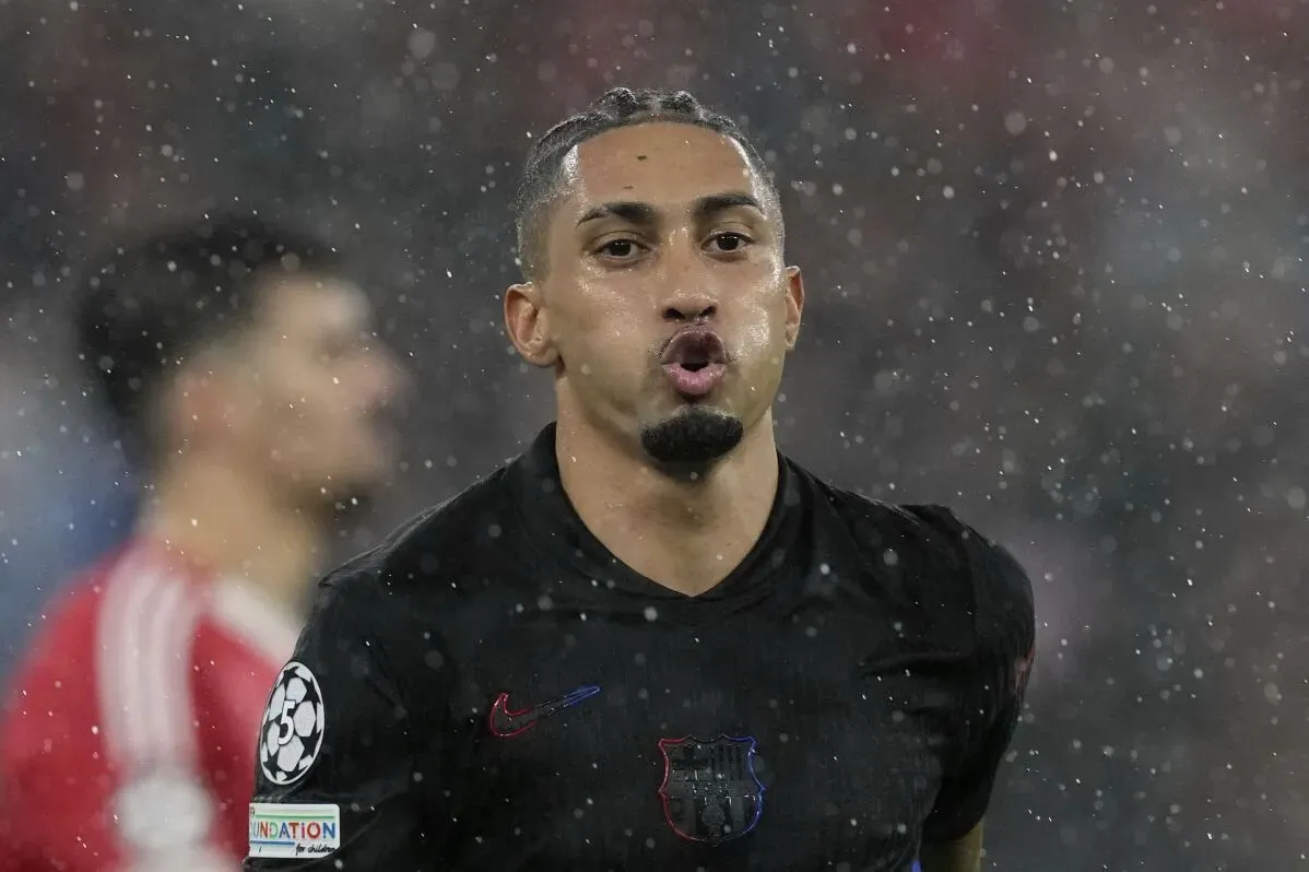 لاعب برشلونة يحتفل بتسجيل هدف في مباراة مثيرة ضد بنفيكا، مع ظهور الأمطار حوله، مما يبرز الأجواء الحماسية.