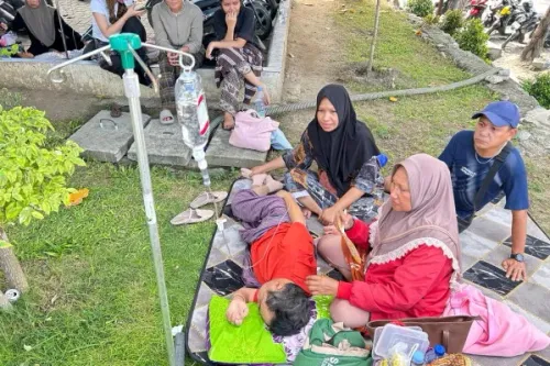نساء يعتنين بمريض يتلقى العلاج عبر التنقيط الوريدي في الهواء الطلق بعد زلزال سولاويزي، مع وجود أشخاص آخرين في الخلفية.