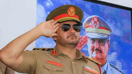 صدام حفتر، نجل القائد العام خليفة حفتر، يؤدي التحية العسكرية، مع صورة والده خلفه، في سياق التحولات السياسية في ليبيا.