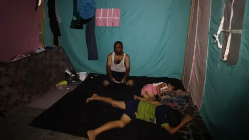 رجل يجلس في خيمة بسيطة مع طفلين نائمين على الأرض، تعكس ظروف المعيشة الصعبة في غزة خلال الحرب والتهجير.