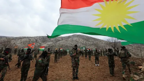مقاتلون أكراد يرتدون زيًا عسكريًا ويستعرضون الأعلام الكردية في منطقة جبلية، في سياق تعزيز الحركة القومية الكردية.